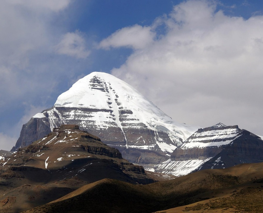 kailash_ynwangjing-mount-kailash-3192640_1280_scaled Snow-capped peak of Mount Kailash rising above rocky foothills under a partly cloudy sky